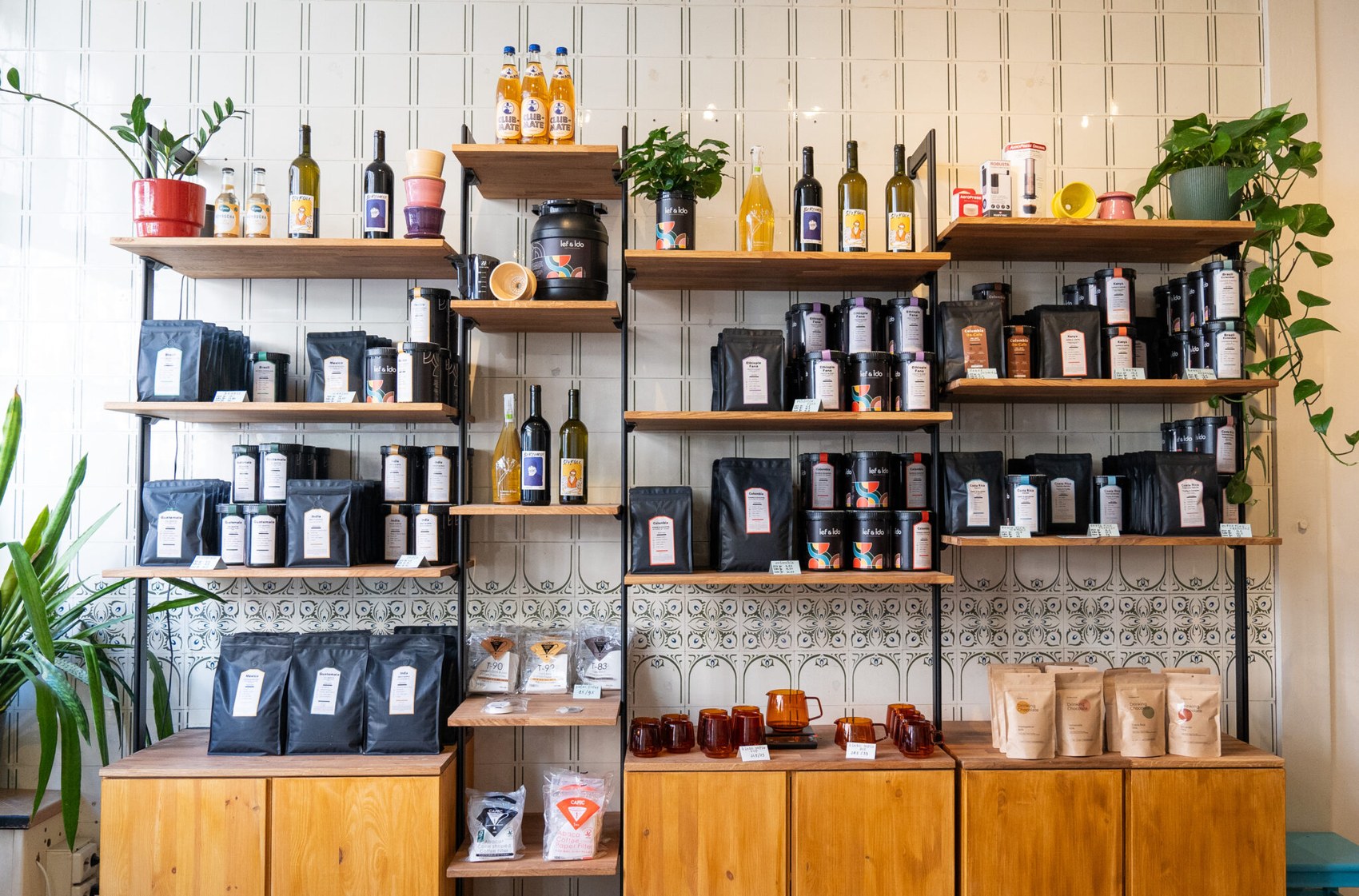 Retail shelving stacked with Ief&Ido bean bags and tins, natural wine, kombucha and brewing gear against patterned tile